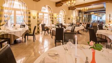 Un restaurant doté de plusieurs tables rondes, chacune recouverte d’une nappe blanche et agrémentée de bougies et de verres à vin.