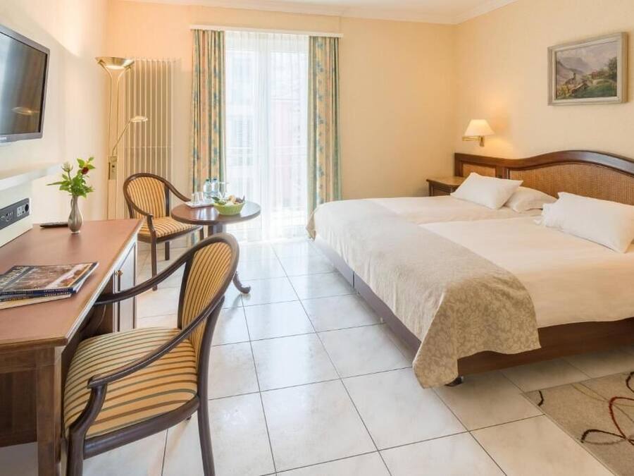 Camera d'albergo con un letto, una scrivania con sedie, una televisione e una finestra con tende.