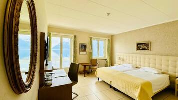 Une chambre d’hôtel avec un grand lit, un bureau, une chaise, une petite table et un grand miroir.