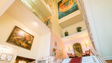 Una majestuosa escalera con alfombra roja que conduce a un rellano con un cuadro grande y un candelabro.