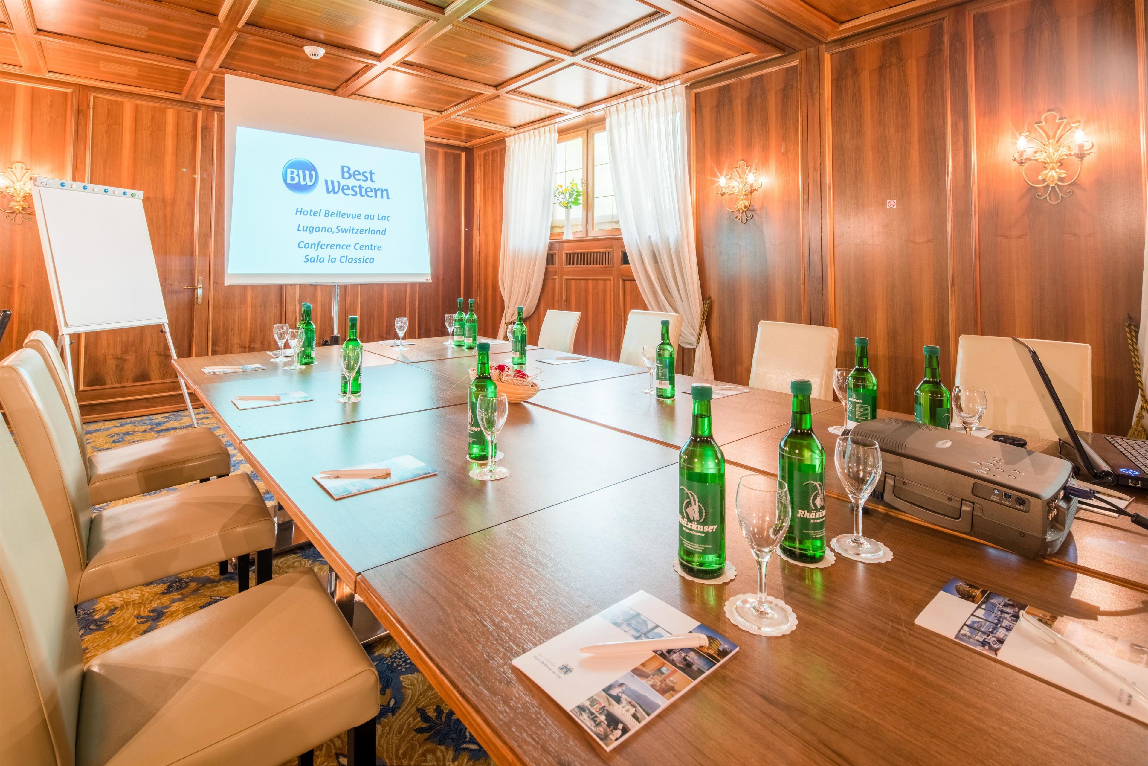 A conference room with a long table, chairs, a projector screen, and a laptop.