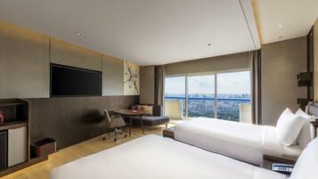 Een hotelkamer met een groot bed, een bureau, een stoel, een televisie en uitzicht over de stad.