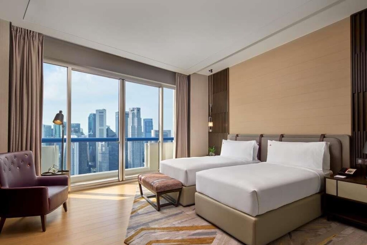 Een hotelkamer met twee bedden, een bank, uitzicht op de stad en een groot raam.