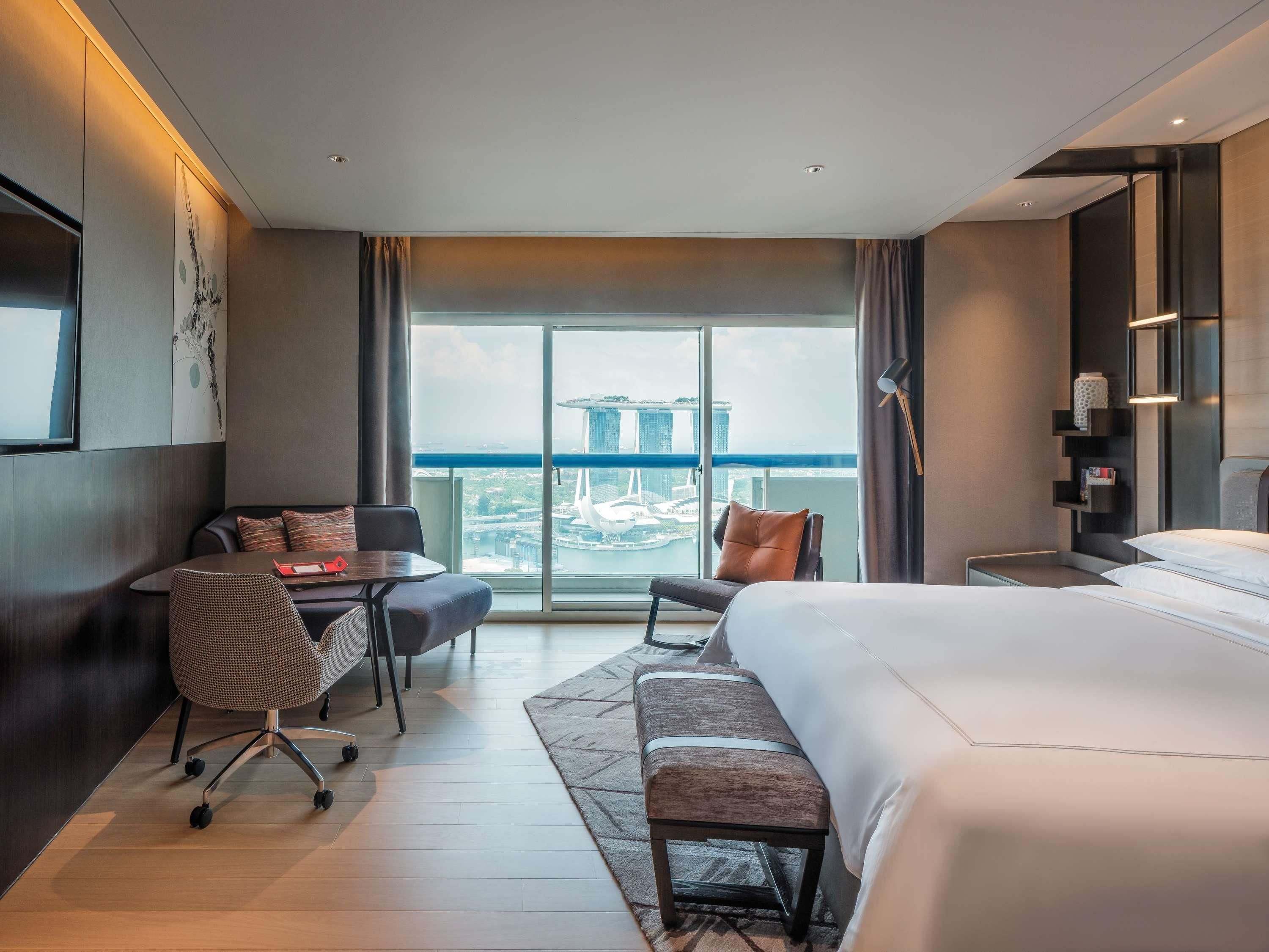 Une chambre d’hôtel moderne avec un grand lit, un bureau, une chaise et une vue sur le paysage urbain.