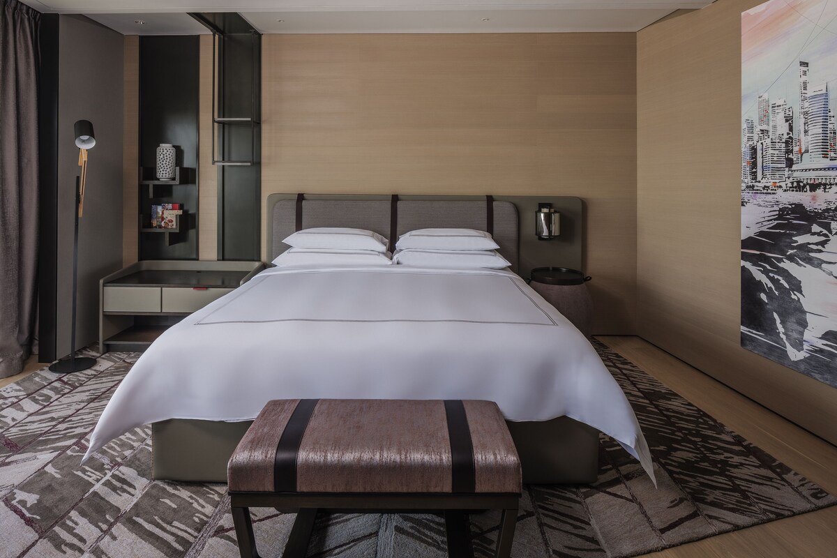 Een hotelkamer met een groot bed, een nachtkastje, een lamp, een boekenkast en een schilderij aan de muur.