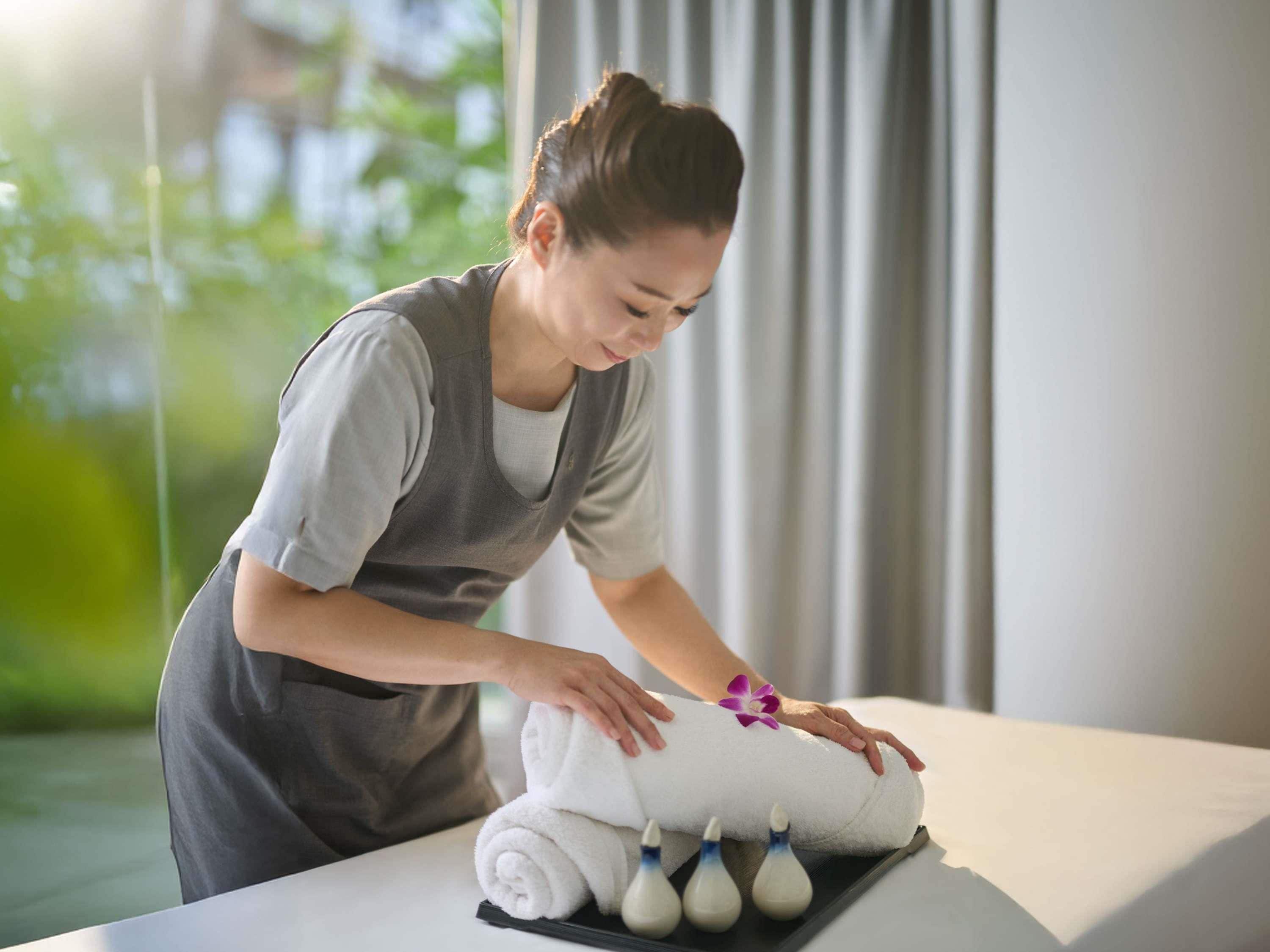 A person attending to a massage table with towels and massage tools.