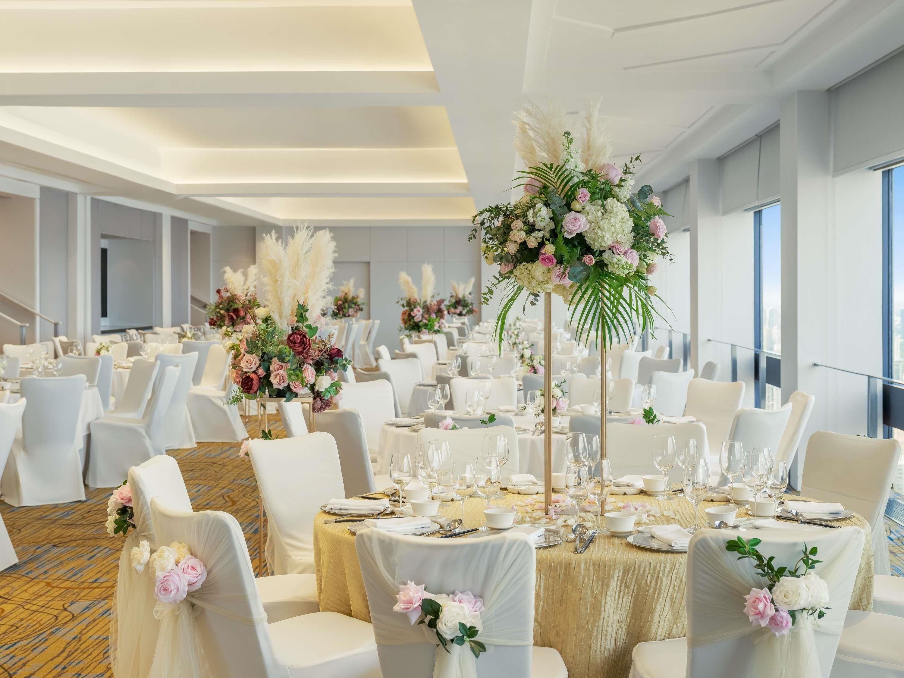 Un salón de banquetes con mesas redondas, sillas blancas y centros de mesa florales.