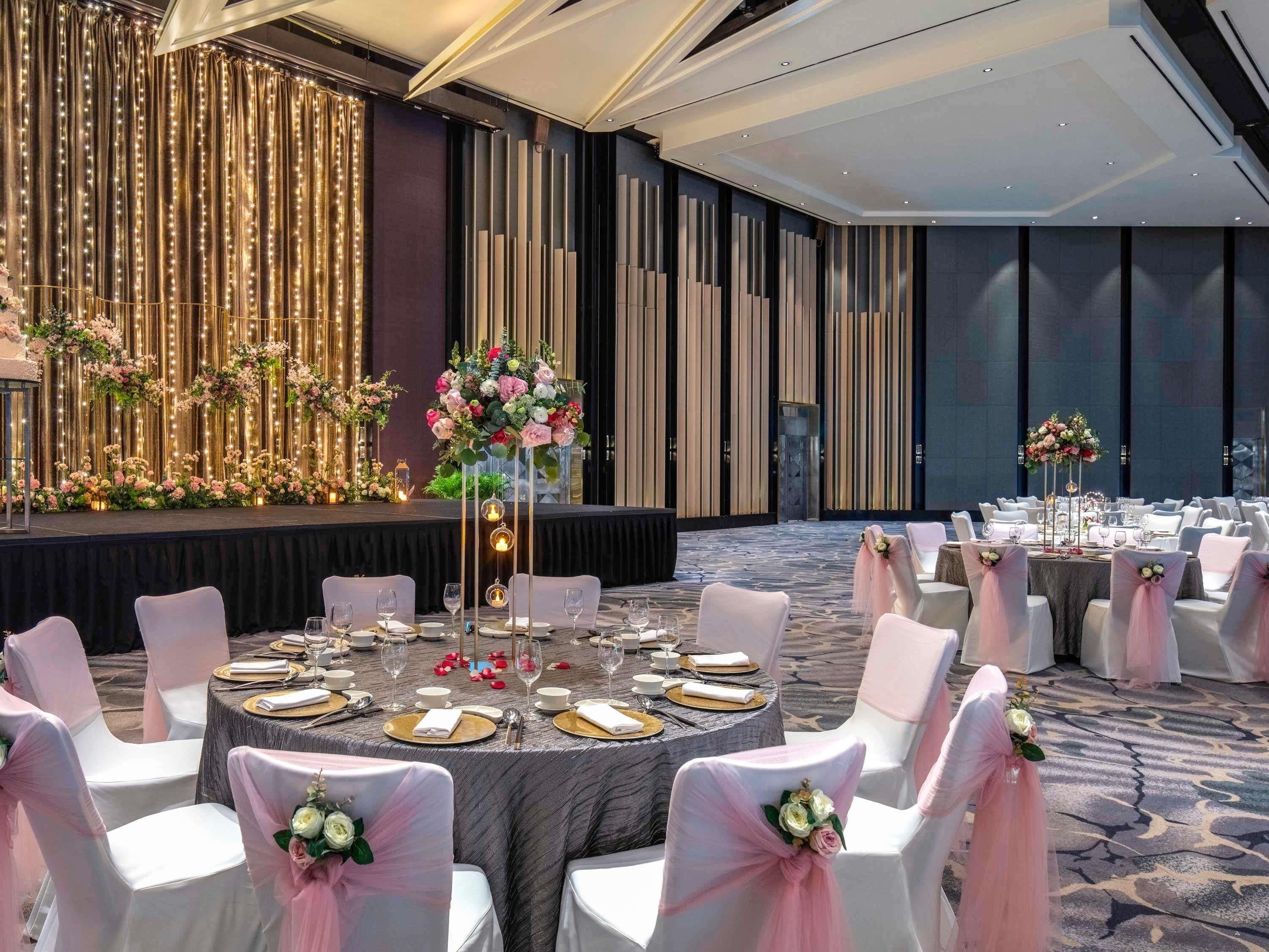 A banquet hall with round tables, white chairs, and floral centerpieces.