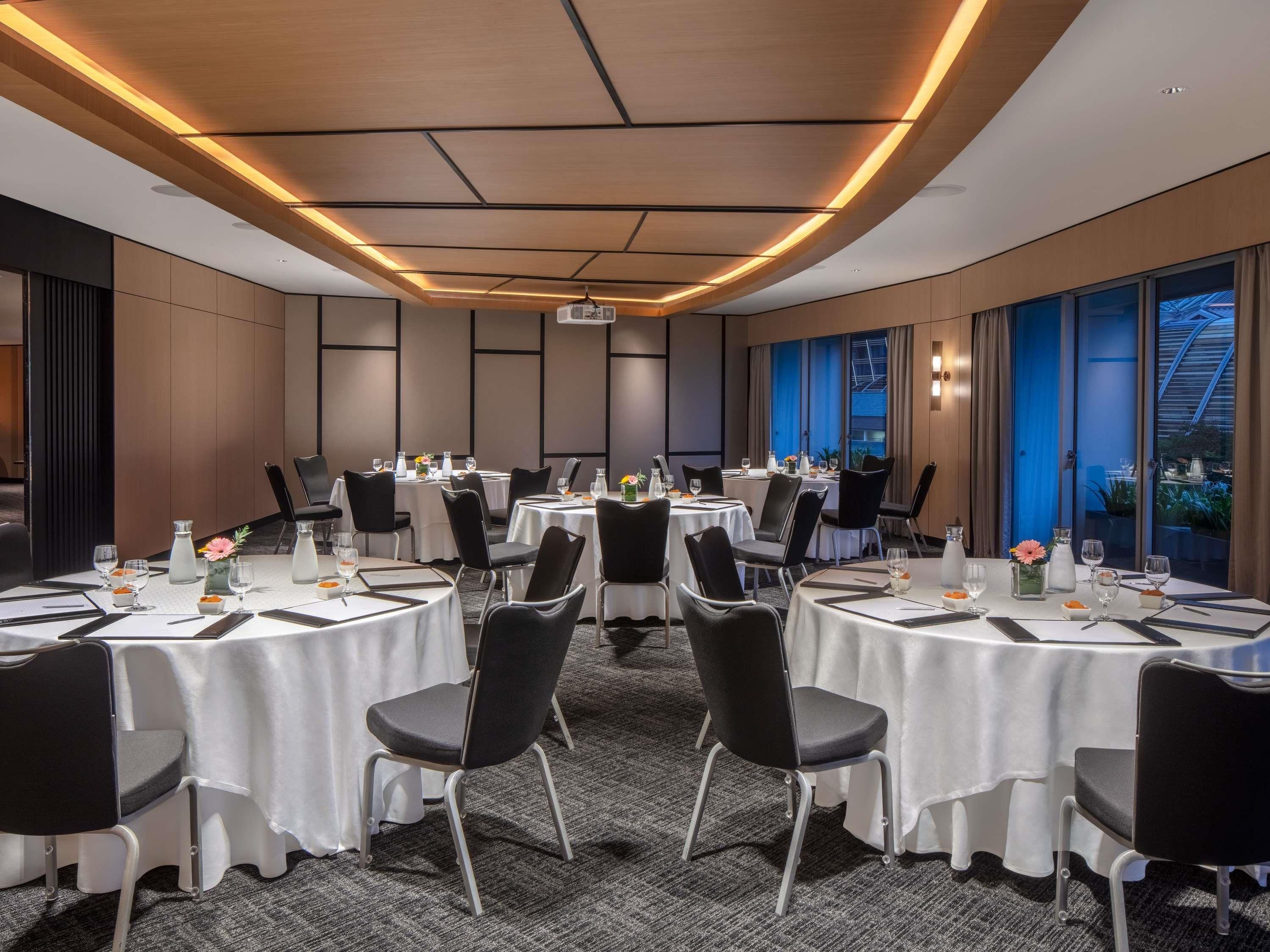 Une salle de conférence avec des tables rondes, des chaises noires et des nappes blanches.