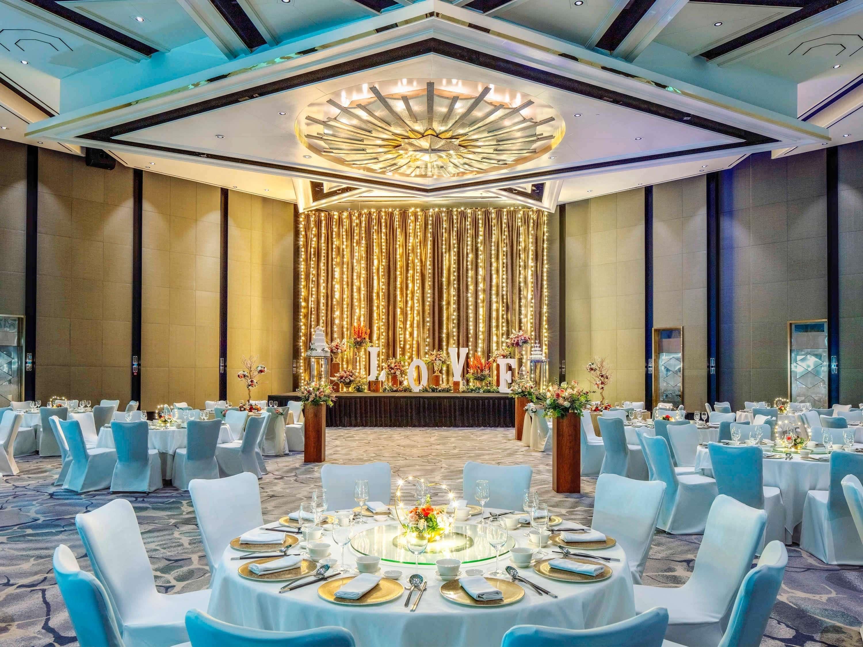 A banquet hall with round tables, white chairs, and a stage with a 'LOVE' backdrop.