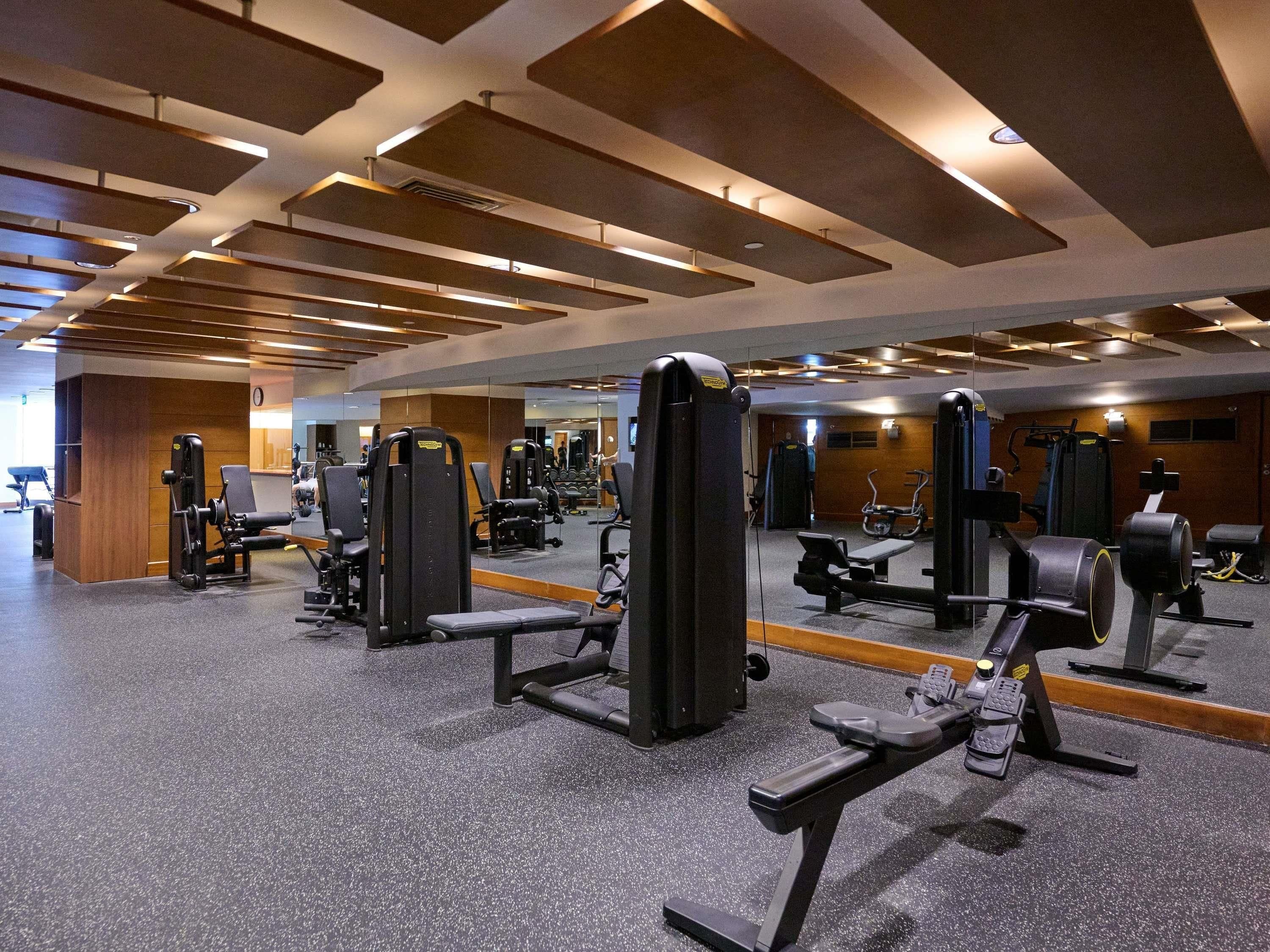Een sportschool met diverse fitnessapparaten, een spiegelwand en een plafond met inbouwspots.