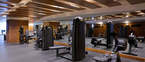Een sportschool met diverse fitnessapparaten, een spiegelwand en een plafond met inbouwspots.