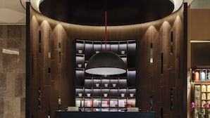 Un espace d’accueil moderne avec un comptoir central, un grand luminaire suspendu et un mur composé d’étagères où sont exposés divers objets.