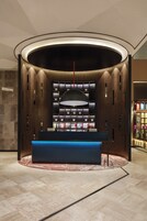 Una zona de recepción moderna con un mostrador central, una lámpara colgante grande y una pared de estanterías que exhiben objetos.