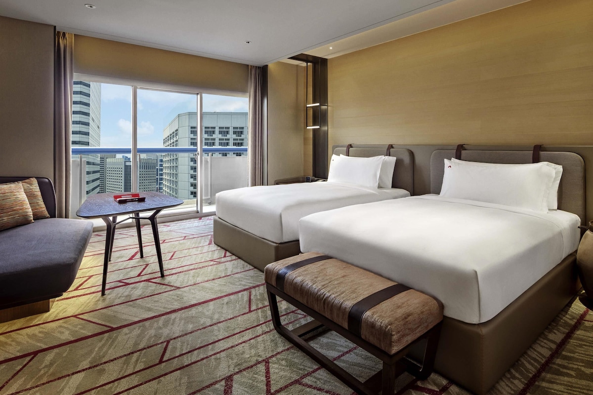 Une chambre d’hôtel avec deux lits, un canapé, une petite table et une vue sur le paysage urbain.