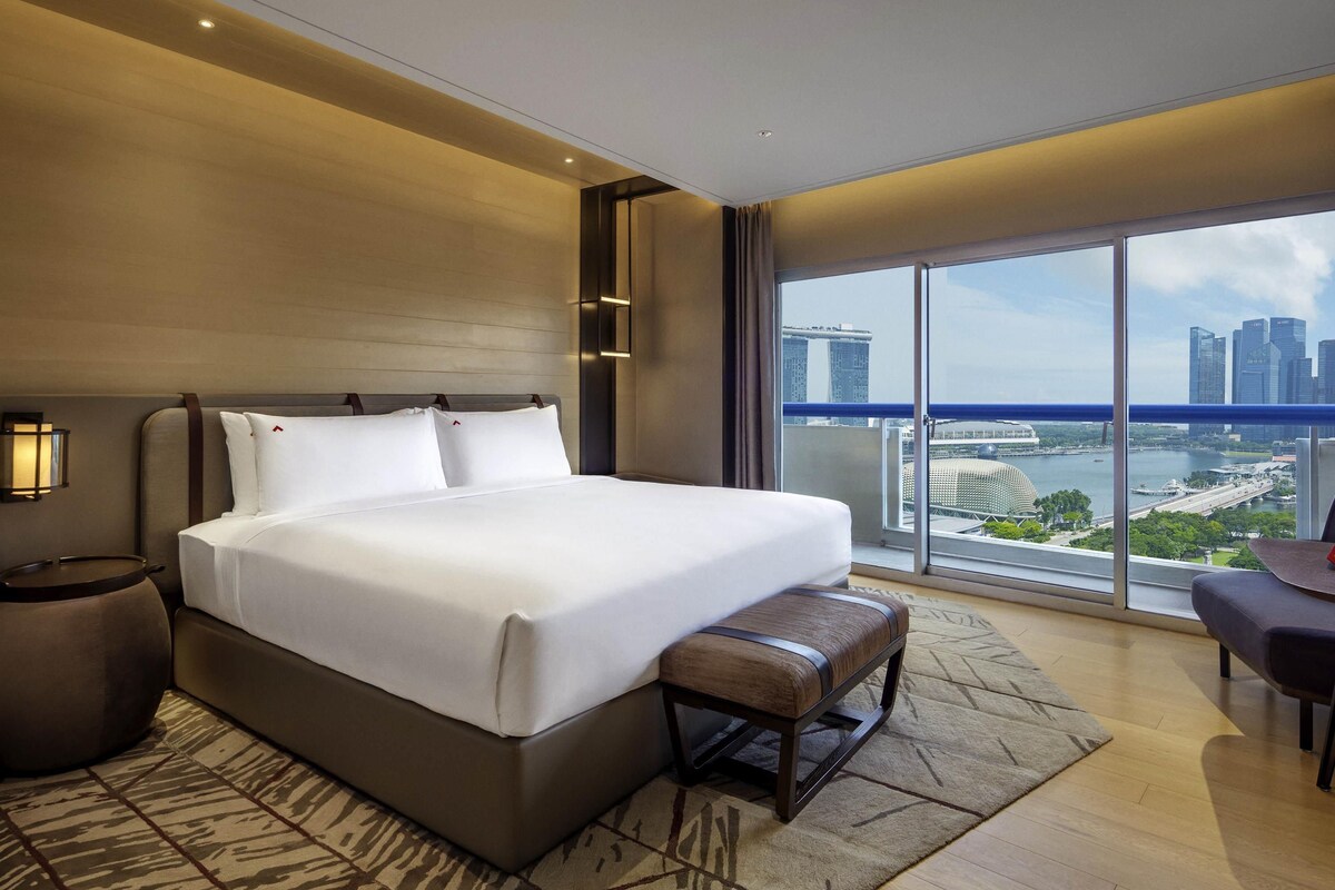 Een moderne hotelkamer met een groot bed, een bank, een bureau en uitzicht op een stadsbeeld.