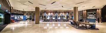 Un vestíbulo amplio con un área de estar central, una recepción y un bar.