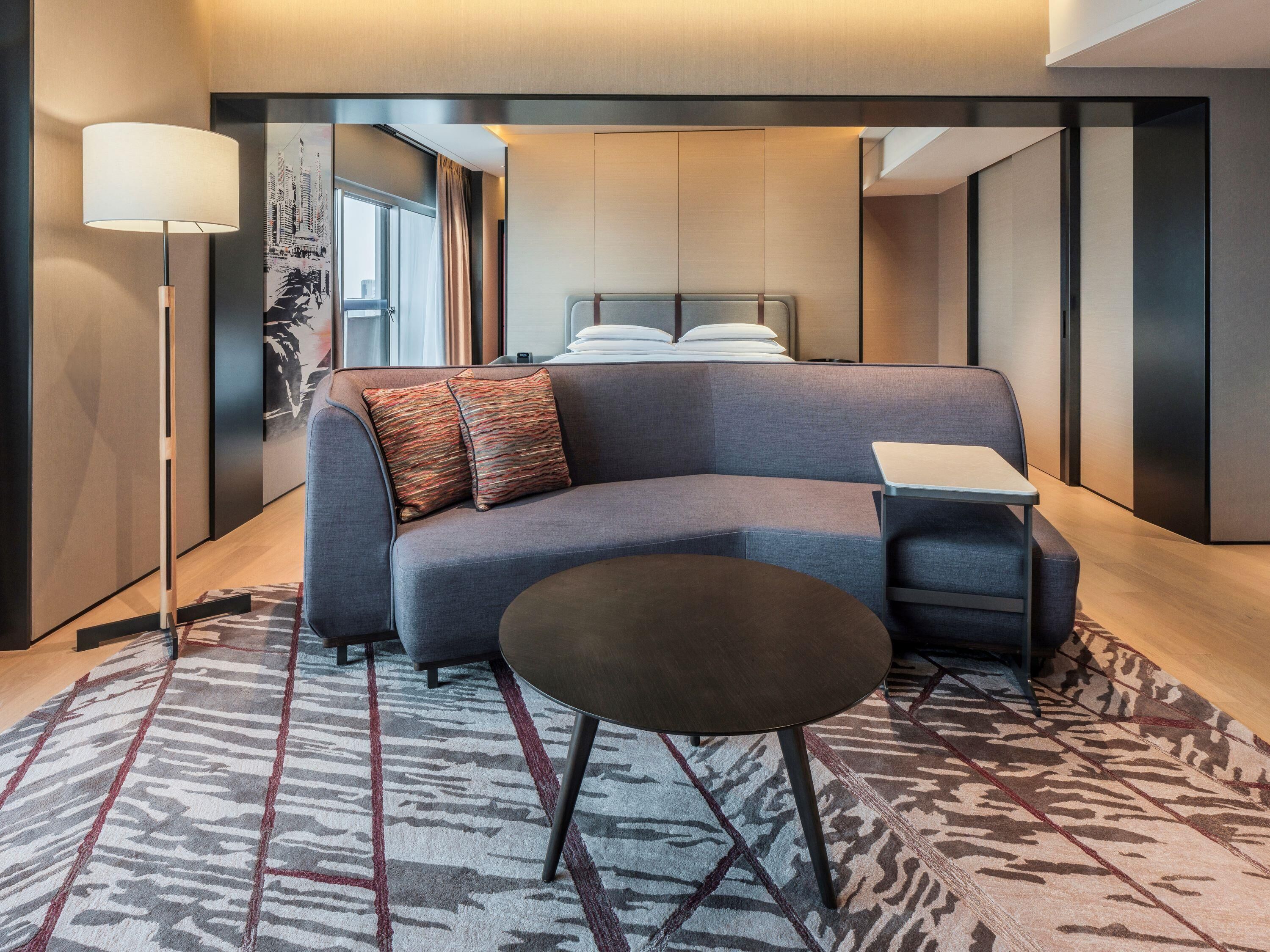 Een moderne hotelkamer met een bank, een klein tafeltje, een lamp en een kamerkleed met dessin.