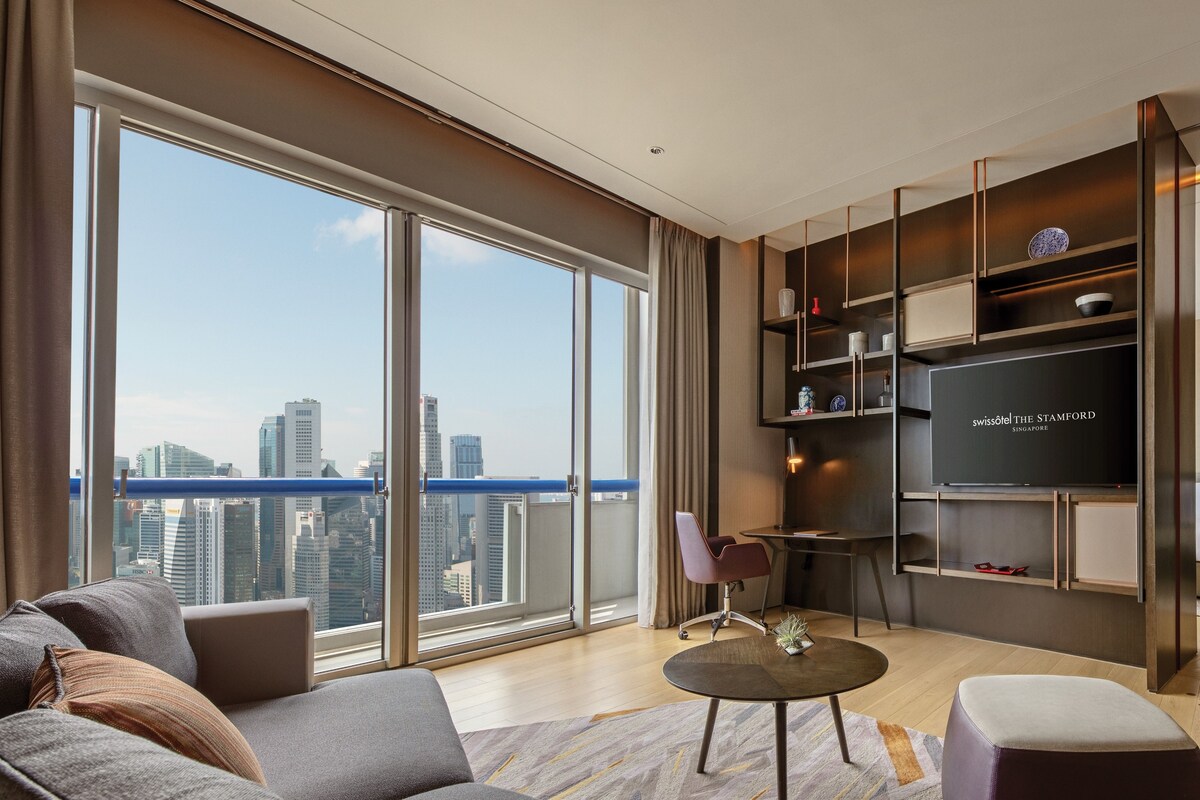 Een moderne woonkamer met een groot raam, een bank, een salontafel en een televisie op een plank.