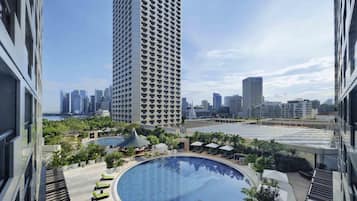 Un edificio de gran altura con piscina en la azotea, rodeada de sillones de descanso y follaje.