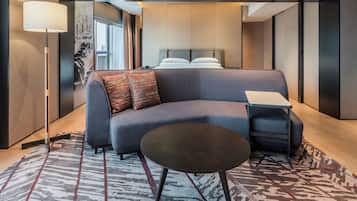 Une chambre d’hôtel moderne avec un canapé, une petite table, une lampe et un tapis à motifs.