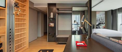A modern hotel room with a bed, exercise equipment, a desk, and a view of the city.