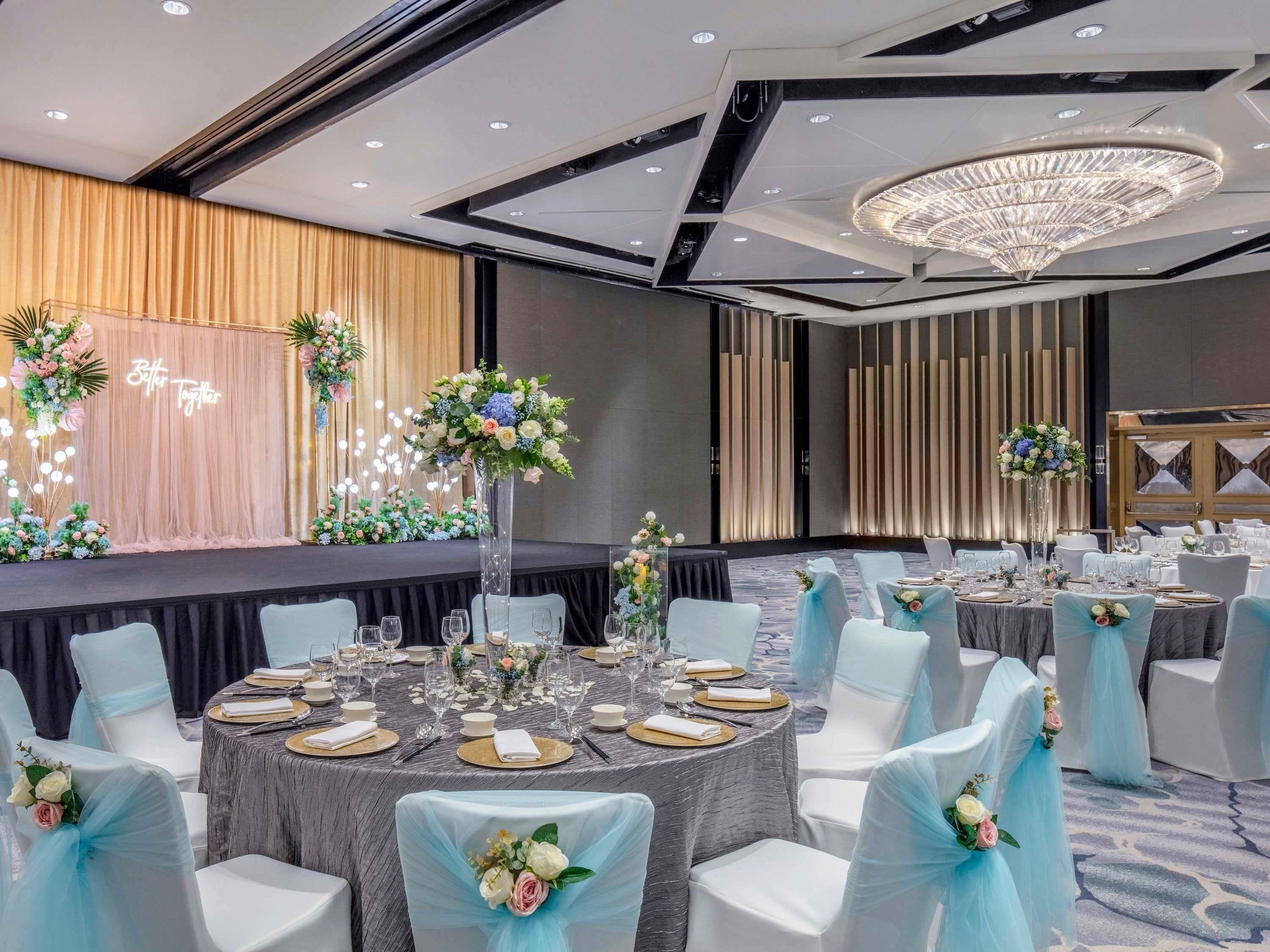A banquet hall with round tables, white chairs, and floral centerpieces.