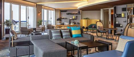 Una sala de estar moderna con un sofá, un sillón y una mesa de centro, un comedor con sillas y una cocina al fondo.