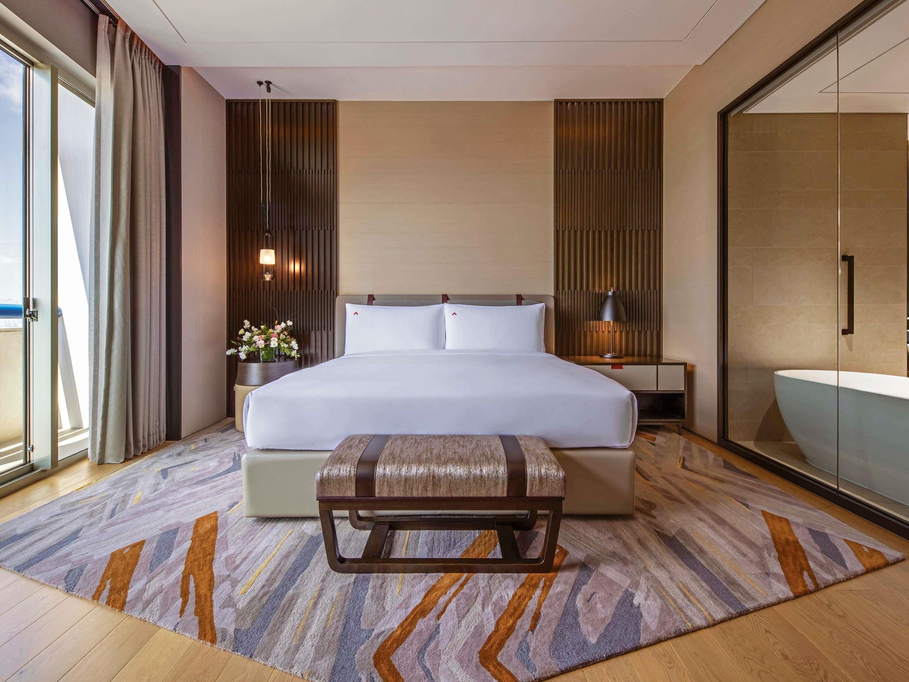 Een moderne hotelkamer met een groot bed, een nachtkastje met lamp, een badkamer met glazen wanden en uitzicht door het raam.