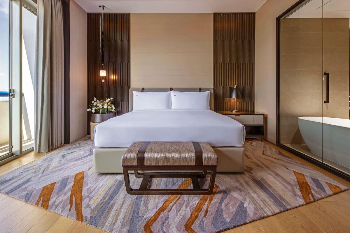 Een moderne hotelkamer met een groot bed, een nachtkastje met lamp, een badkamer met glazen wanden en uitzicht door het raam.