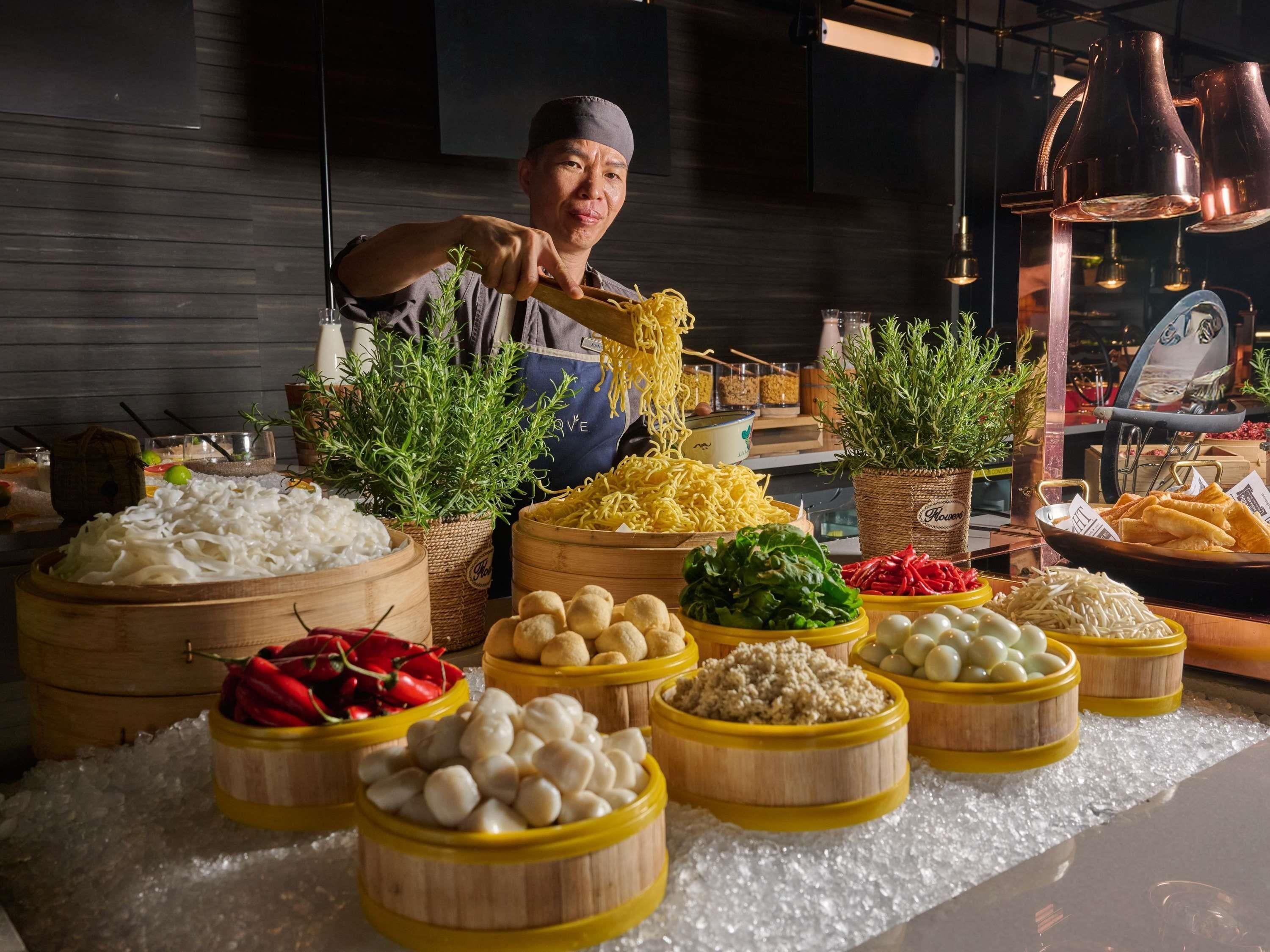 A buffet with various food items and a person serving noodles.
