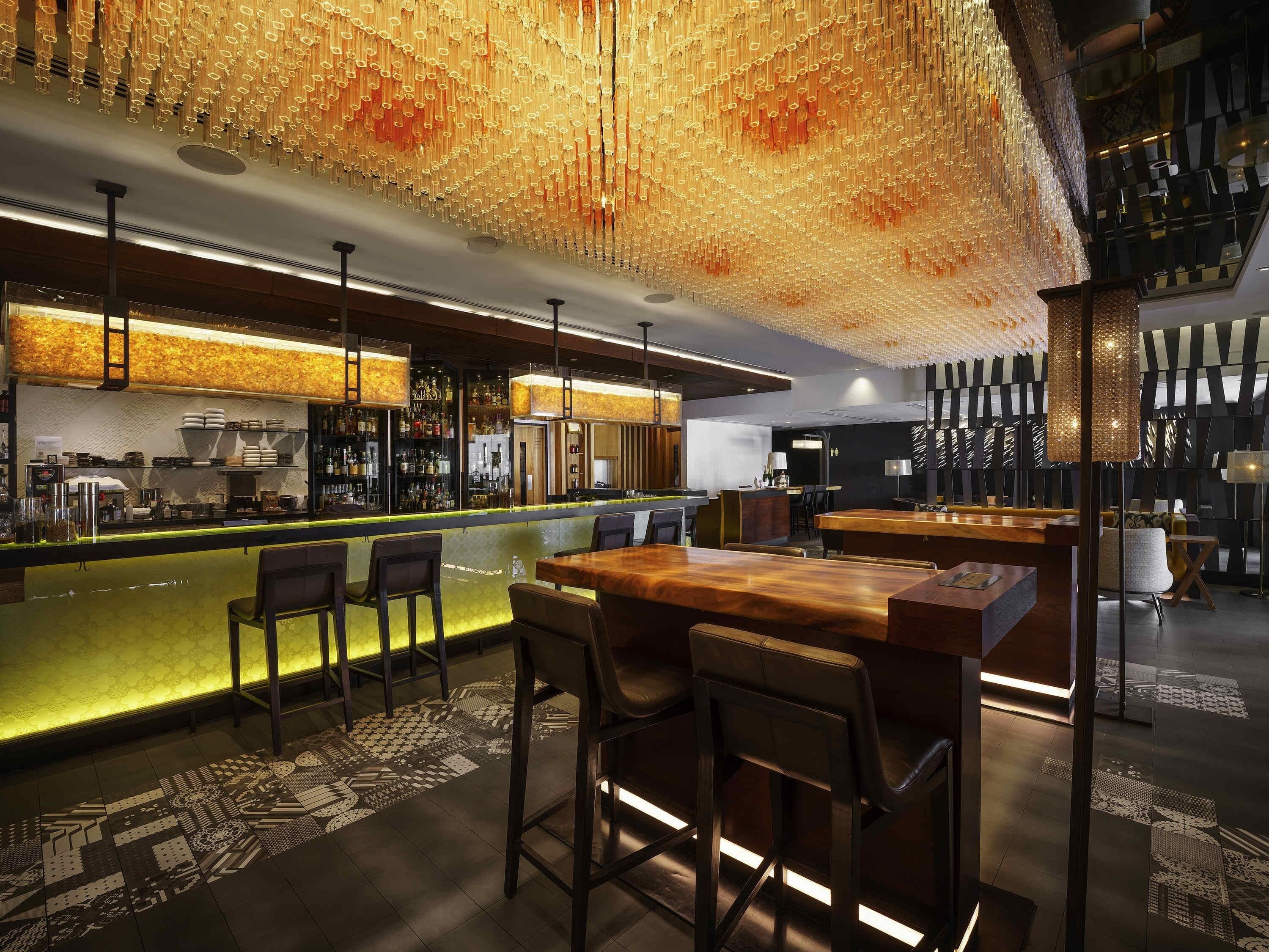 Een moderne bar met een versierd plafond, barkrukken en een toonbank met diverse flessen.