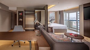 A modern hotel room with a sofa, a small table, a desk, a bed, and a TV.