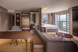 A modern hotel room with a sofa, a small table, a desk, a bed, and a TV.