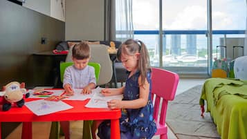 Dos niños dibujando en una mesa roja, con vista a la ciudad.