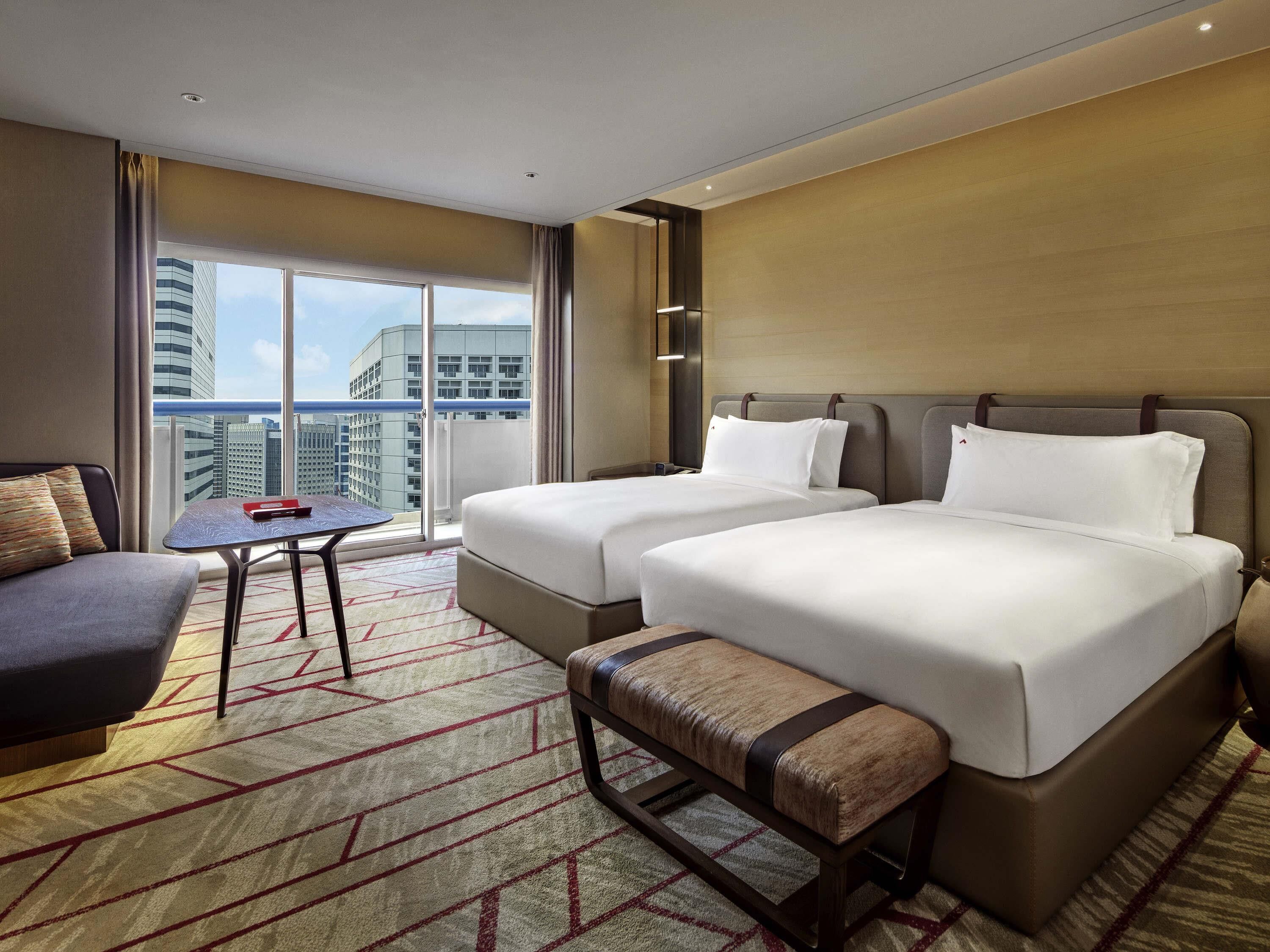 Een hotelkamer met twee bedden, een bank, een tafeltje en uitzicht op de stad.