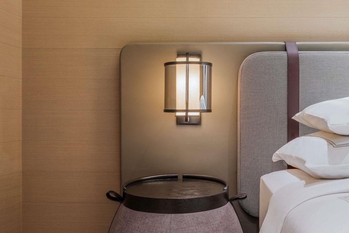 Une chambre d’hôtel moderne avec un mur en bois, une table ronde avec un pot de fleurs, une lampe fixée au mur et un lit avec des oreillers.