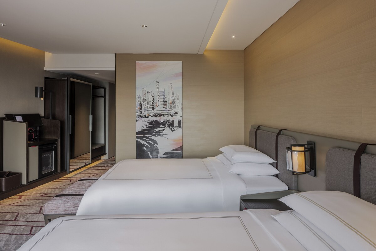 Een hotelkamer met twee bedden, een groot schilderij aan de muur, een bureau met een computer en een lamp.
