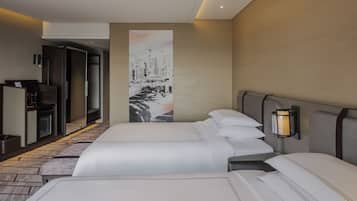A hotel room with two beds, a large painting on the wall, a desk with a computer, and a lamp.