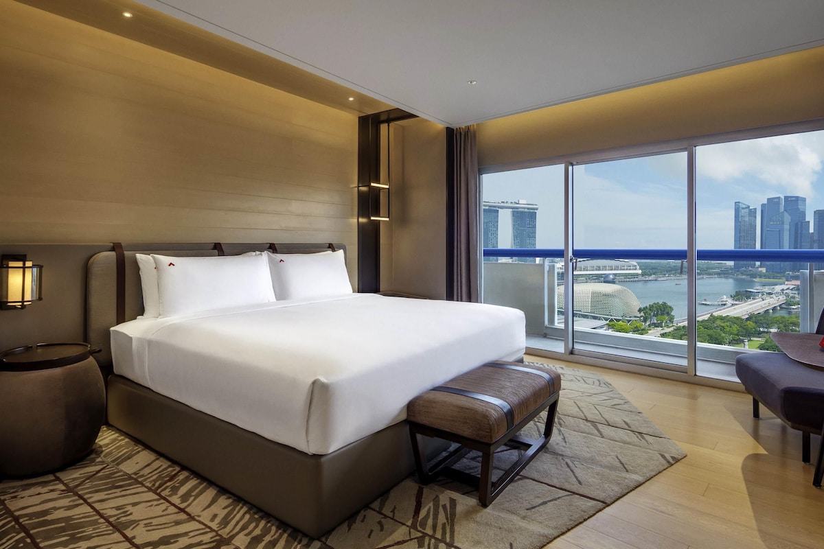 Une chambre d’hôtel moderne avec un grand lit, une banquette, un bureau et une vue sur le paysage urbain.
