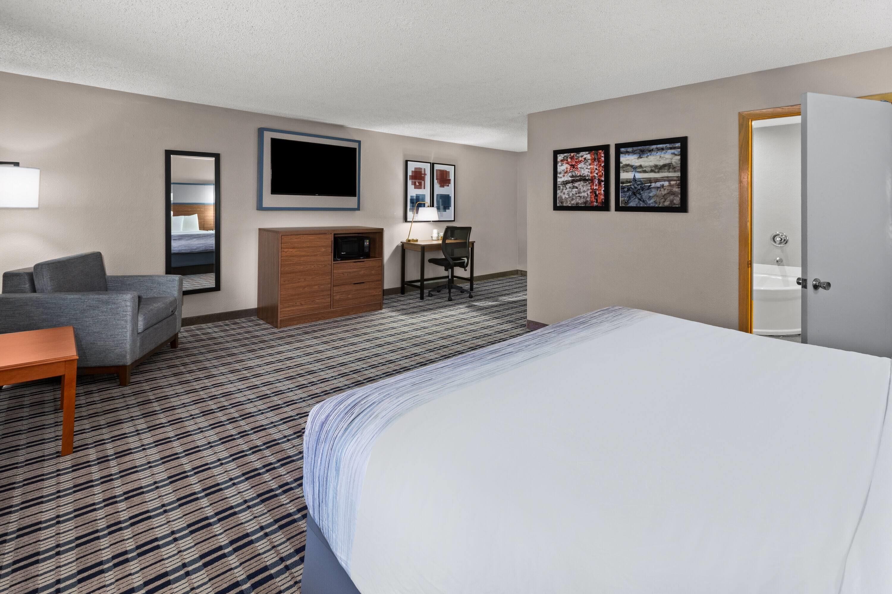 Habitación de hotel con cama, escritorio, silla, televisión y obras de arte en las paredes.