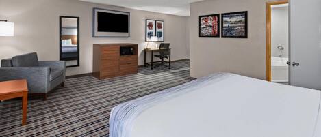 Habitación de hotel con cama, escritorio, silla, televisión y obras de arte en las paredes.