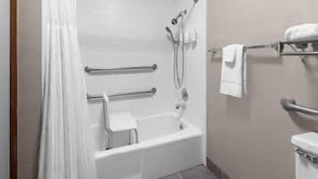 A bathroom with a white bathtub, a shower with a handheld showerhead, a grab bar, a step stool, and a towel rack with a white towel.