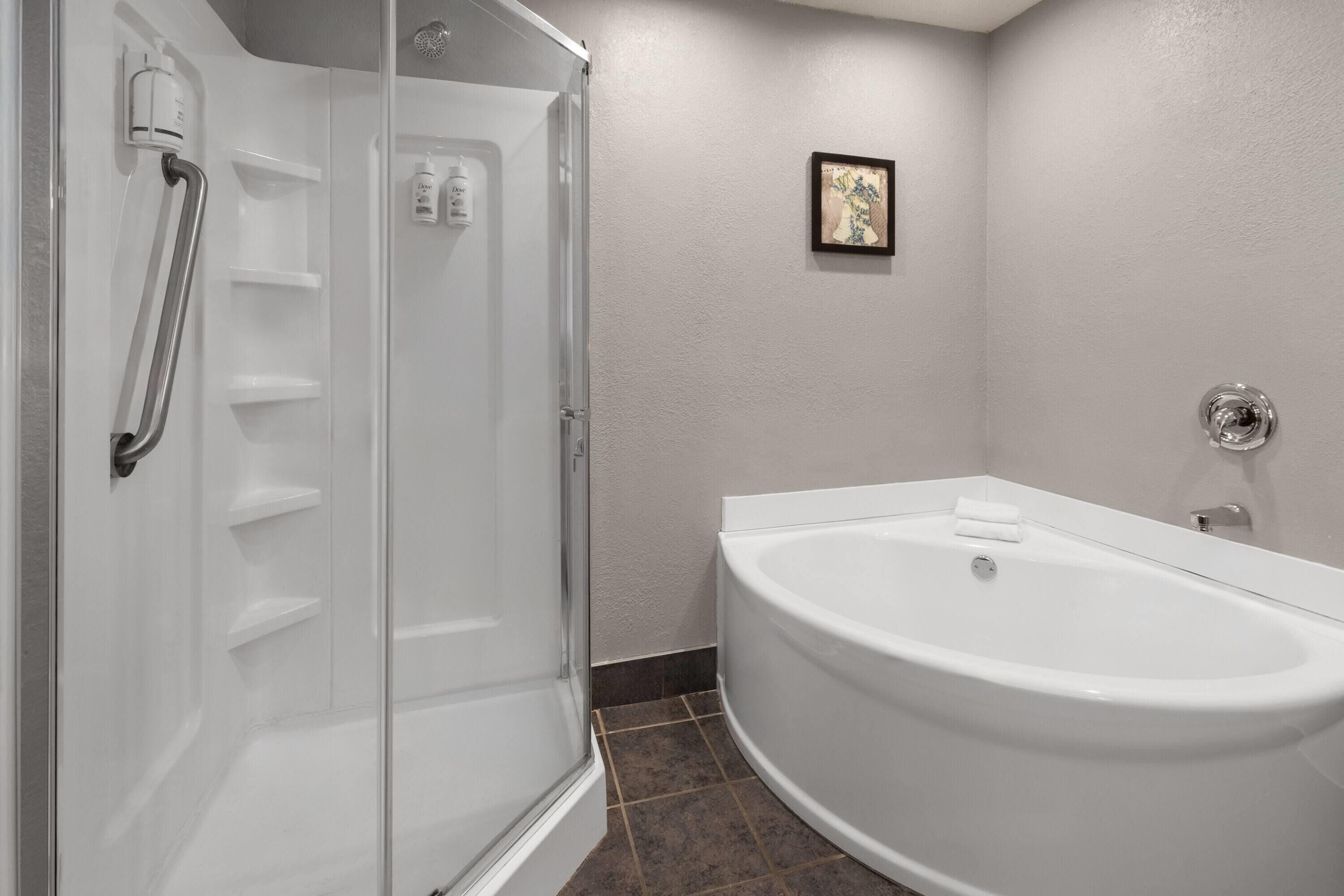 A modern bathroom with a glass-enclosed shower, a white bathtub, and a framed picture on the wall.