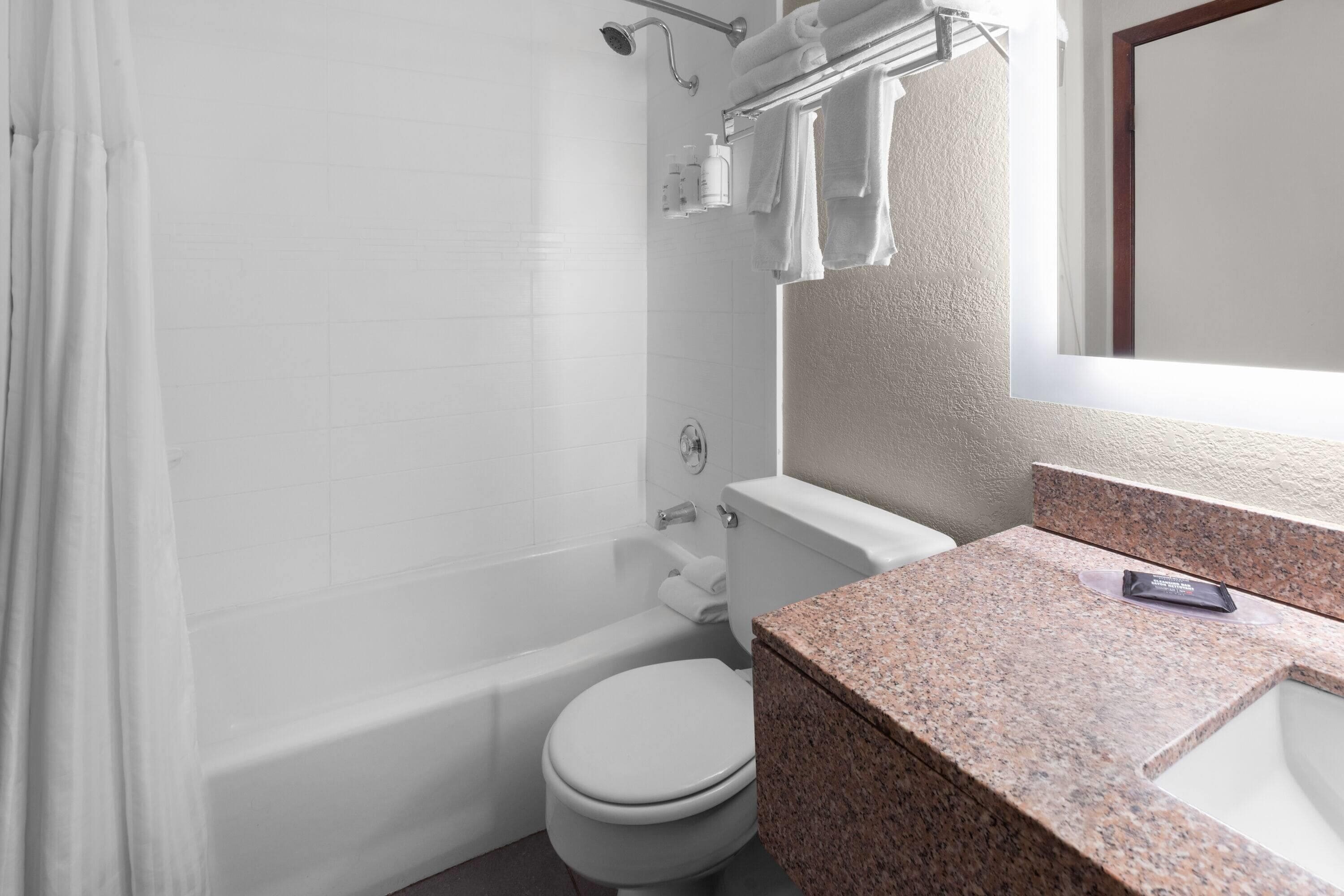 A bathroom with a white toilet, a bathtub, and a granite countertop.