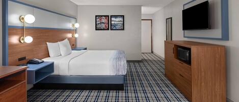 Quarto de hotel com cama, mesa de cabeceira, abajur, televisão de tela plana e carpete estampado.