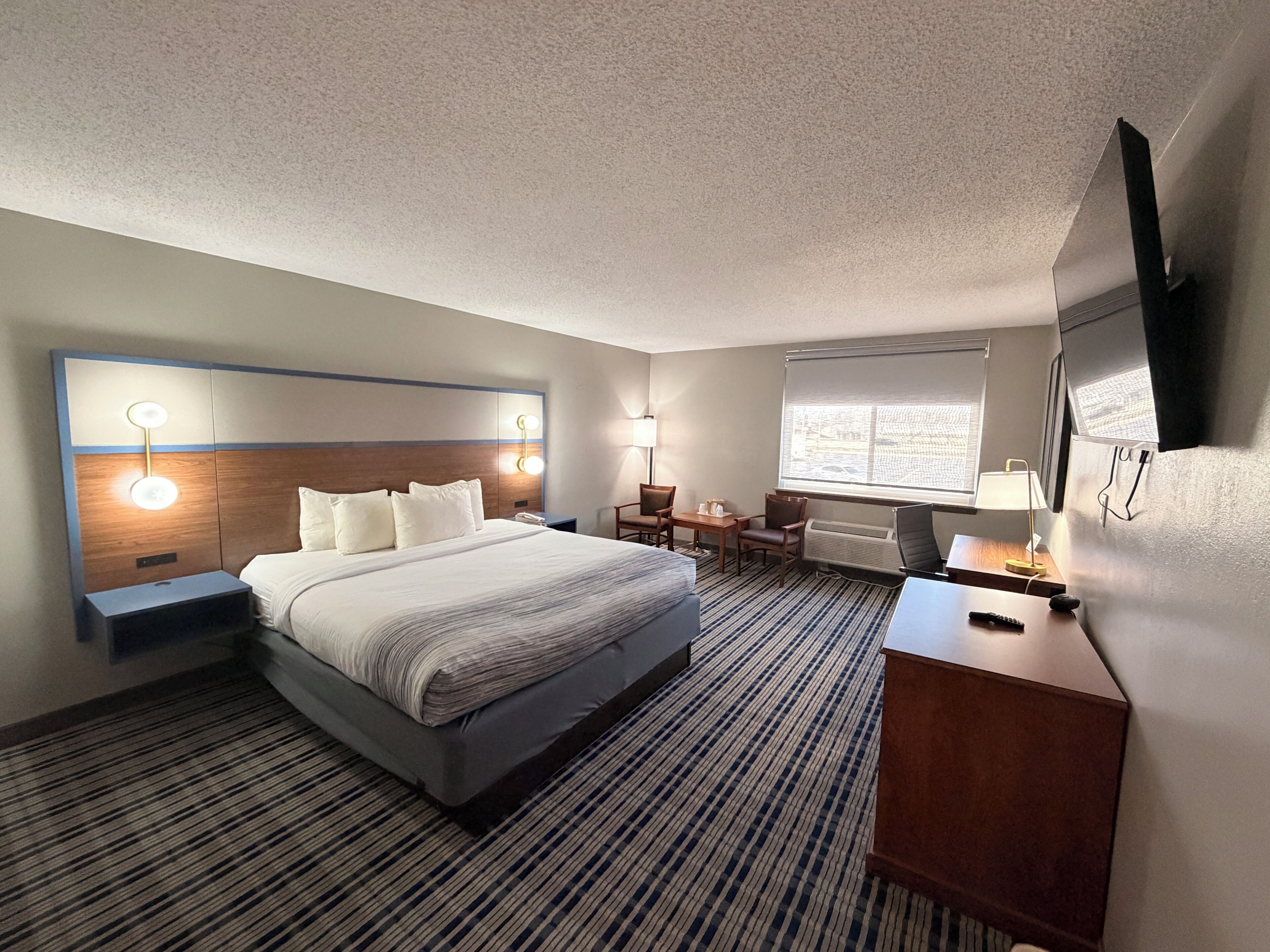 Hotelkamer met een groot bed, nachtkastjes, een bureau met stoel, een televisie en een raam.