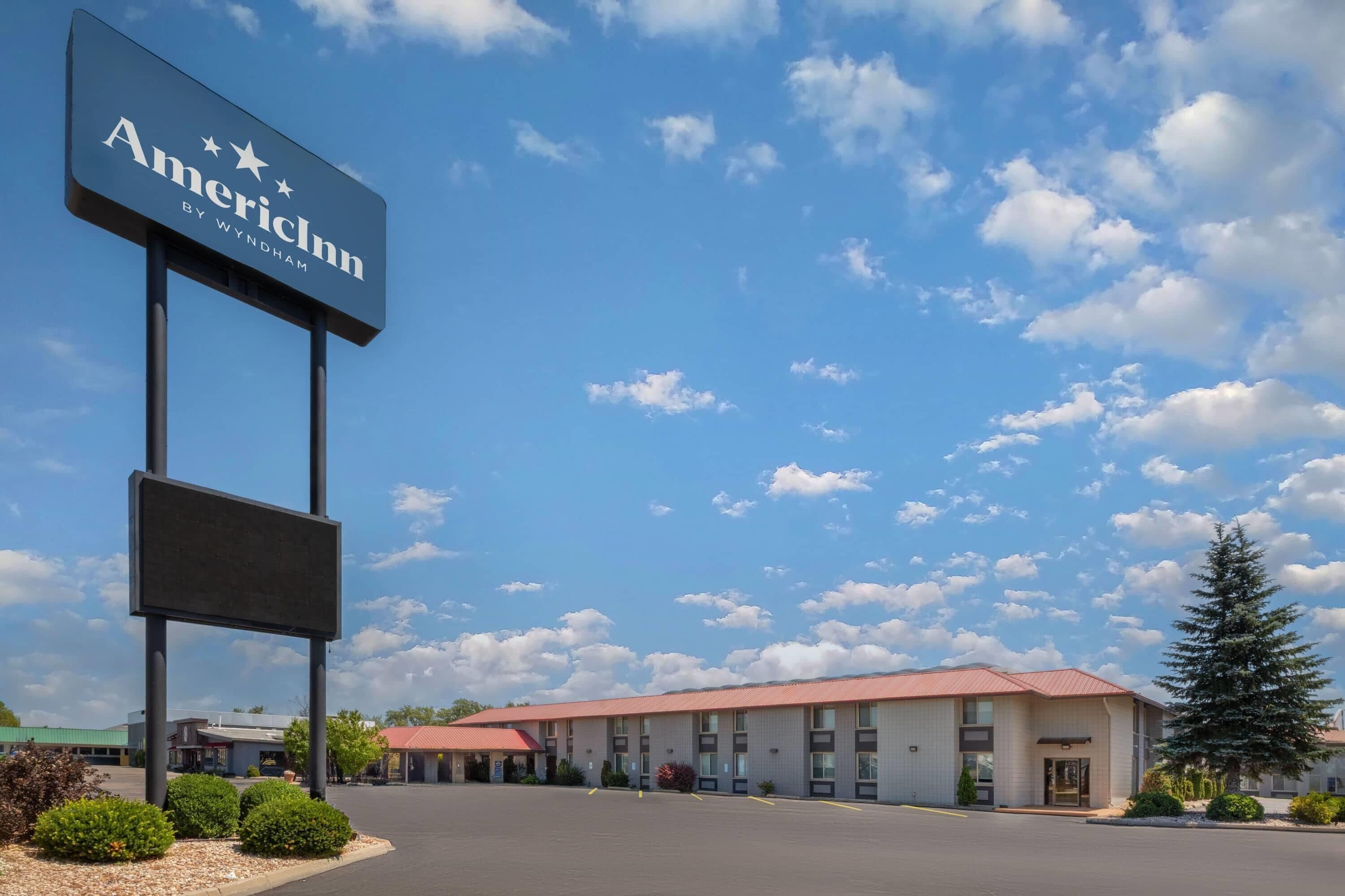 A hotel with a large sign, a parking lot, and a building with a red roof.