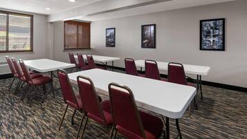 A conference room with white tables and red chairs, large windows with blinds, and framed pictures on the walls.