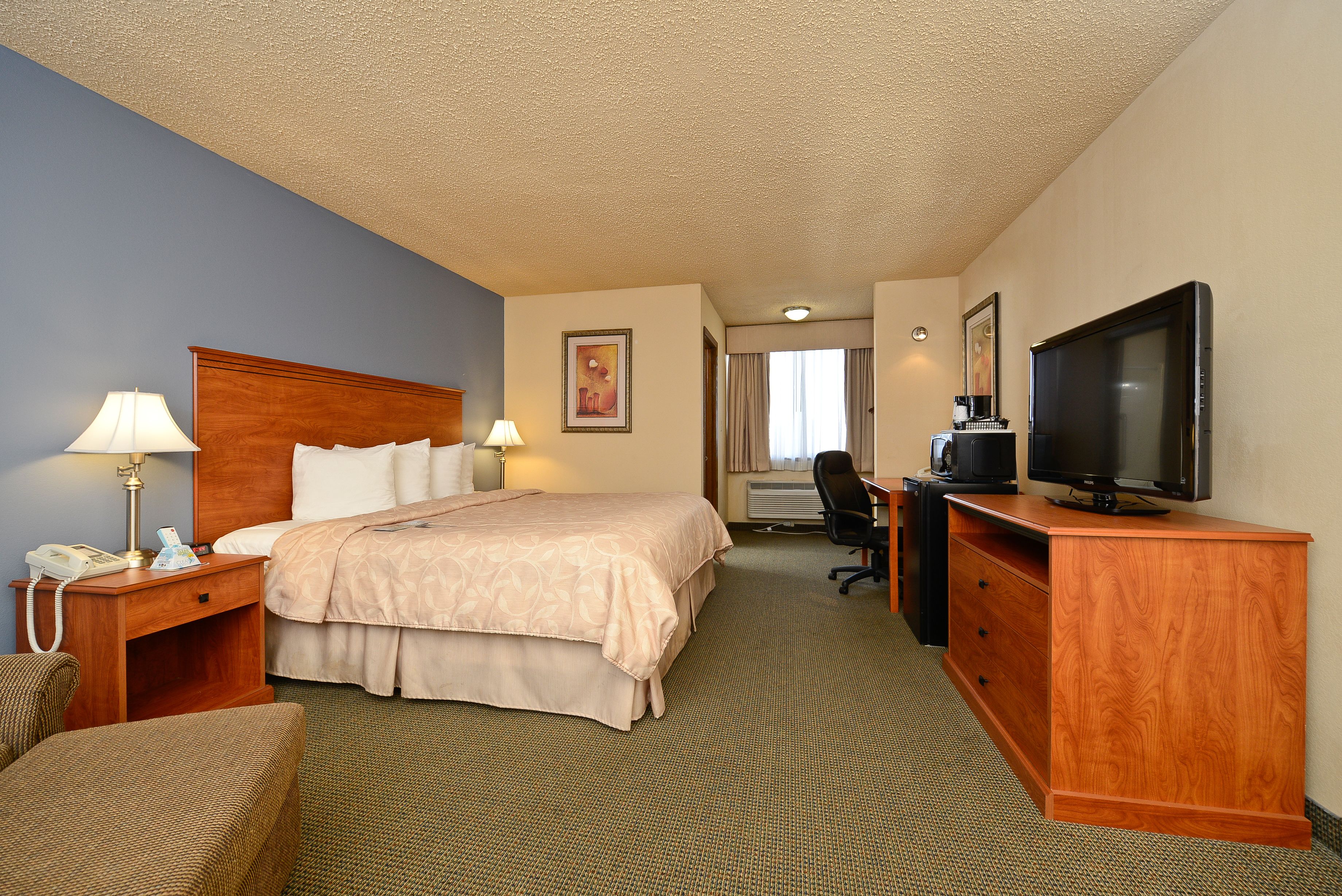 A hotel room with a bed, a desk, a chair, a television, and a desk lamp.